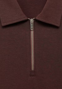 Material tricotat de culoare maronie cu fermoar metalic argintiu parțial deschis dedesubtul unui guler pliat pe un articol de îmbrăcăminte.