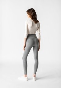 Helle graue Leggings aus elastischem Material mit einem hohen Bund. Getragen mit einem figurbetonten cremefarbenen Oberteil und weißen Sneakers.
