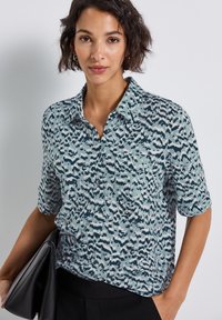 Camicia a maniche corte con bottoni di colore azzurro chiaro e motivo astratto scuro, dotata di taschino sul petto e realizzata in tessuto morbido e leggero.