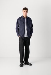 Marineblå langermet skjorte med knapper og to brystlommer, kombinert med mørk denimbukser og svarte sko. Enkelt design, ensfargede farger.