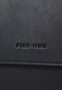 Cuir noir texturé avec des bords surpiqués ; présente le texte en relief "PIER ONE." Design simple et rectangulaire axé sur la fonctionnalité.