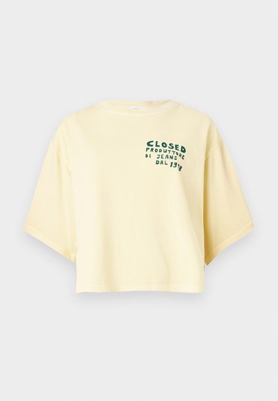 T-shirt jaune en coton à manches courtes et coupe oversize, avec un texte graphique vert sur la partie gauche de la poitrine. Design simple avec une coupe décontractée.