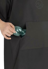 Black garment with a large pocket. A hand inserts a clear, textured water bottle, showing the item's functionality and design.