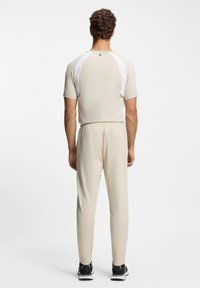 Beige activewear outfit with a fitted short-sleeve top and tapered pants. White accents on shoulders. Material appears smooth and lightweight.