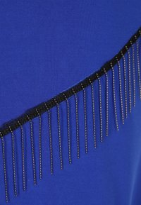 Koninklijkblauwe stof met een horizontale zwarte bies, versierd met verticale metalen kraalfranje, die textuur en detail laat zien.