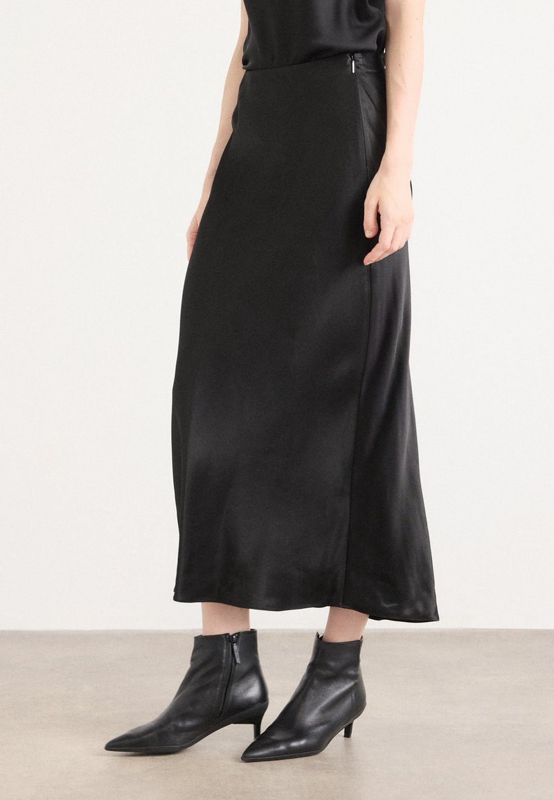 Svart satin midi-skjørt med glatt tekstur og sidelommer, sammen med svarte lær spisse ankelstøvletter med lav hæl.