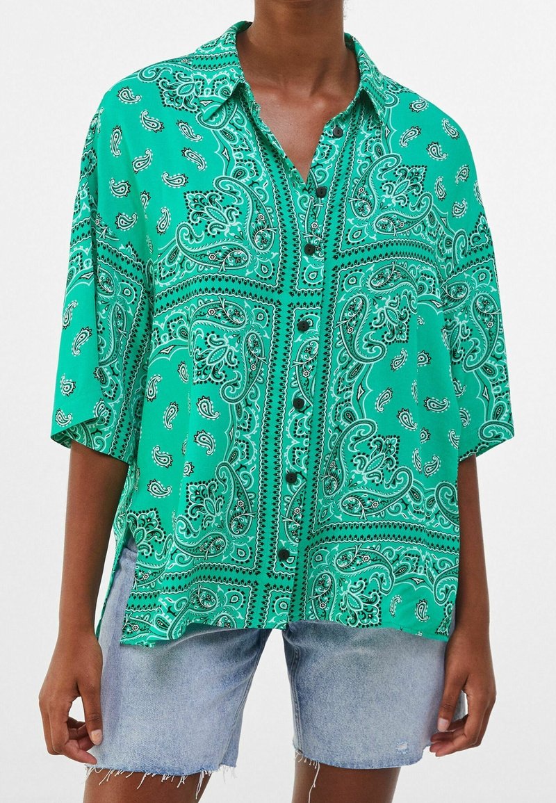Green paisley-patterned shirt with short sleeves, button-up design, and side slits. Made of smooth fabric with a glossy finish.