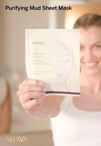Mascarilla de barro purificante AHAVA en un paquete color crema con un gráfico de cara simple y acentos morados, con un diseño limpio y minimalista.