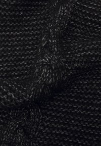 Czarna dzianina o teksturowym wzorze, prezentująca skręcone warkocze oraz różną grubość przędzy, tworząc głębię i wymiar.