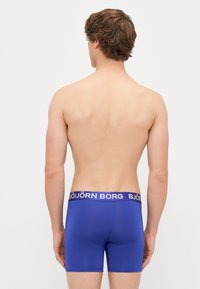 Niebieskie bokserki wykonane z gładkiego materiału z szerokim elastycznym paskiem w talii, na którym w kontrastowych kolorach widnieje nazwa "BJÖRN BORG".