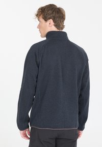 Tumma harmaa fleece-takki, jossa on korkea kaulus, pitkät hihat ja litteät saumat. Ominaisuuksiin kuuluu sileä rakenne ja rento istuvuus.