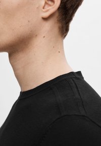 Pull en tricot noir avec un col rond, un col côtelé et des coutures d'épaule texturées. Le tissu semble doux avec une finition lisse.