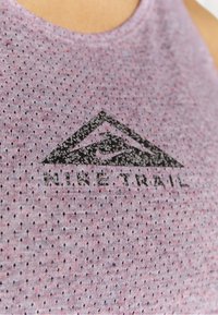 Primo piano di una canotta sportiva in rete viola con il logo Nike Trail nero che presenta un design montano e il logo swoosh di Nike.