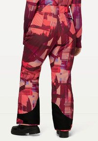 Pantalons de ski colorés avec un motif géométrique en teintes de rouge et de rose, avec un accent noir à l'ourlet. Fabriqués à partir d'un tissu résistant.