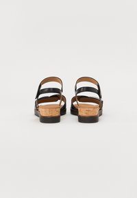 Black leather sandals with two adjustable straps, cork heels, and a textured black sole. Minimalist design with open back and toe.