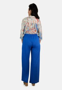 Pantalones azules fluidos con un corte holgado y cinturilla elástica, combinados con una camisa de manga larga ligera y estampada que presenta remolinos en rojo y azul.