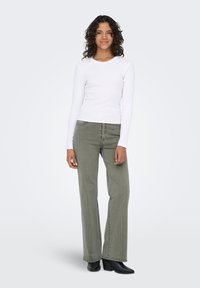 Άσπρη ριμπ μπλούζα με μακριά μανίκια συνδυασμένη με χακί παντελόνι καμπάνα και μαύρα μποτάκια αστραγάλου, παρουσιάζεται πάνω σε ουδέτερο φόντο.