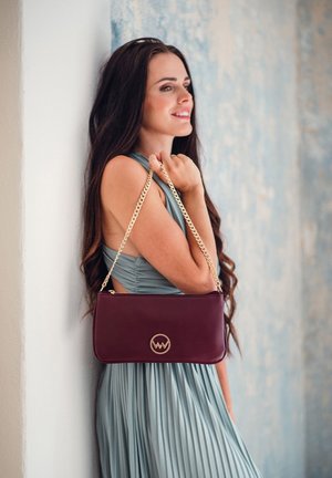 Burgundy leather handbag with a gold chain strap, featuring a circular gold logo. Smooth texture with a rectangular shape and zipper closure.