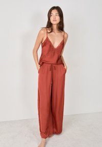 Roestkleurige satin top met kantafwerking, gecombineerd met losse, wijde broekspijpen met een elastische tailleband en zijzakken.