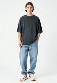 Palaidų kirpimų pilkas marškinėliai su trumpomis rankovėmis, derinami su šviesiai mėlynais tiesiais džinsais ir baltais sportbačiais su raudonais ir tamsiai mėlynais akcentais.