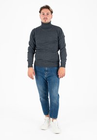 Maglione color grigio scuro a collo alto con design aderente, abbinato a jeans azzurri a sigaretta e sneakers bianche. Texture semplice e liscia.