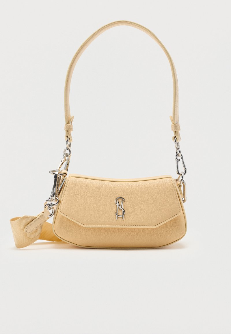 Sac à bandoulière en cuir beige avec logo en métal argenté à l'avant, bandoulière amovible et forme rectangulaire arrondie sur un fond uni.