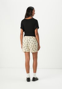 Haut noir ample à manches courtes associé à un short crème avec un motif géométrique. Des chaussures noires et des chaussettes blanches complètent la tenue.