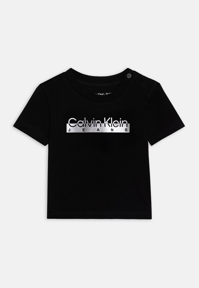 Black cotton T-shirt with short sleeves. Features a silver printed "Calvin Klein JEANS" logo across the chest and snap button detail on the shoulder.