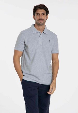 Polo shirt gris à manches courtes avec col, deux boutons et logo brodé. Porté avec un pantalon bleu marine foncé, texture en coton lisse.