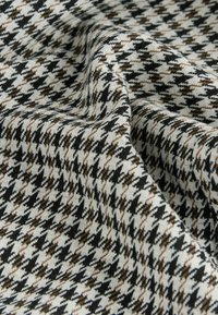 Vævet tekstil med et brunt, sort og cremefarvet houndstooth-mønster, der har en glat, struktureret overflade og en blød drapering.