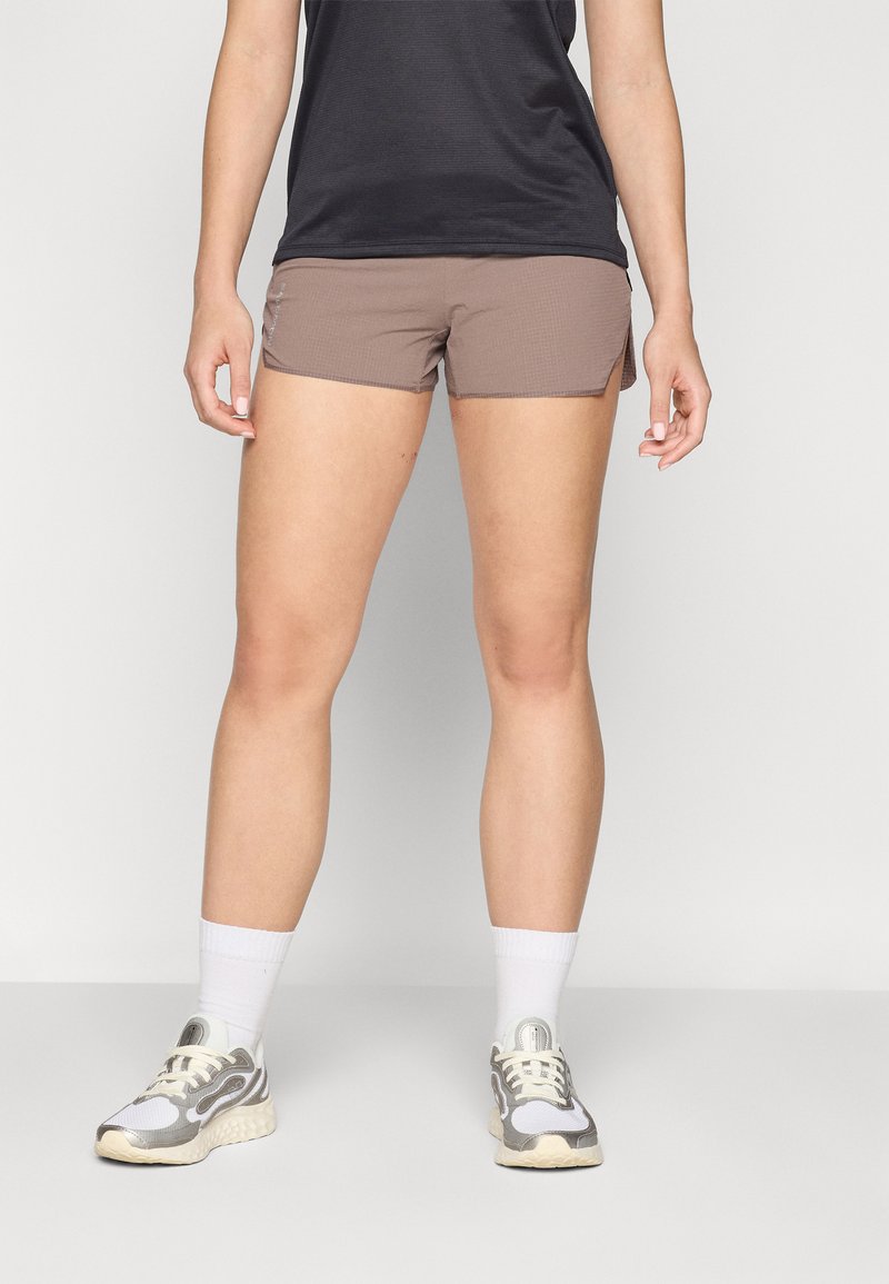 Pantalones cortos deportivos marrones claros con un patrón texturizado, aberturas laterales y un diseño ajustado, combinados con una camiseta negra y zapatillas gris.