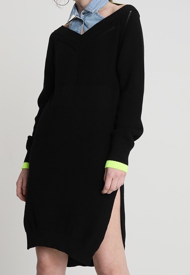 Svart stickad klänning med långa ärmar, V-ringning och sidoklyftor. Har en neongrön accent vid ärmkanterna, texturerad tyg och löst sittande passform.