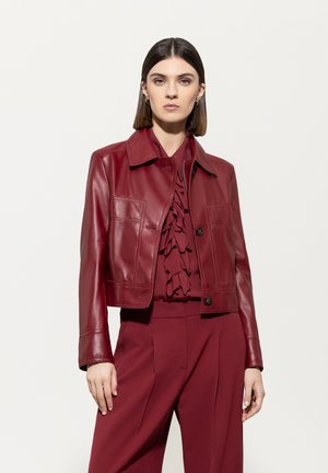 Kürzer roter Lederjacke mit Kragen, Fronttaschen und Knopfverschluss, kombiniert mit einem passenden strukturierten Oberteil und Hosen.
