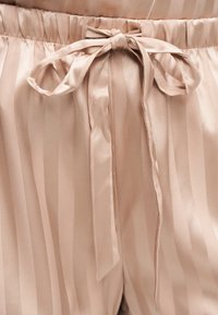 Shorts en satin beige clair avec des rayures verticales et une taille élastique nouée avec un délicat nœud à l'avant.