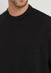 Sort bomulds T-shirt med rund halsudskæring og korte ærmer. Har en lille brystlomme med en syet kant. Glat tekstur.