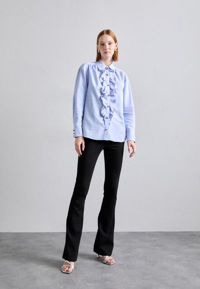 Light blue button-up shirt with front ruffles, paired with black flared pants and silver heeled sandals. Smooth fabric texture.
