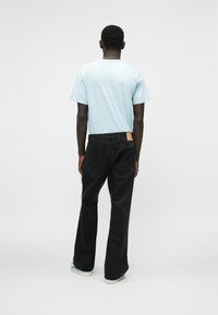 Gaiši zils īsās piedurknes T-krekls kombinēts ar melniem, brīva piegriezuma džinsiem, kuriem ir ādas birka uz aizmugures jostas un kontrastējoši stikli.