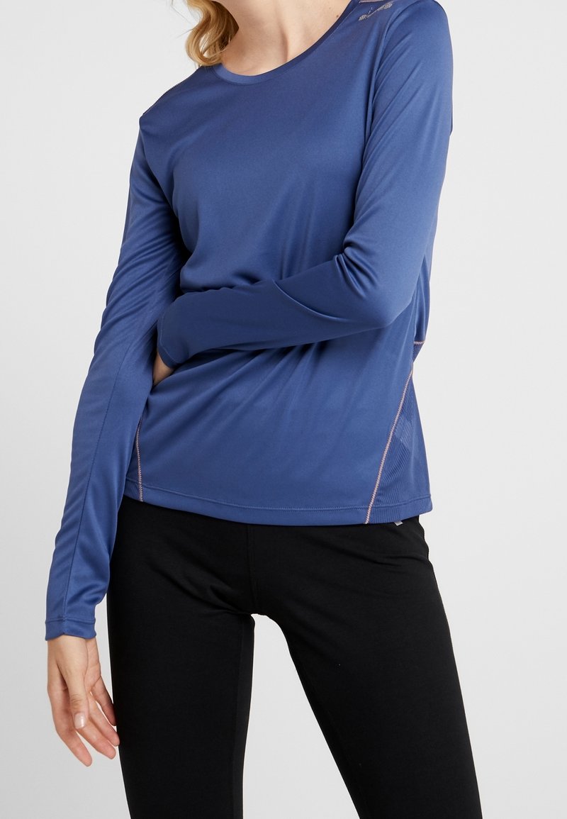 Camiseta deportiva de manga larga en azul, fabricada con tejido que absorbe la humedad. Presenta un cuello redondo y paneles laterales de malla para mayor transpirabilidad.