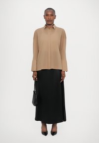 Beige long-sleeve shirt with a pointed collar, paired with a black satin maxi skirt. The outfit includes a textured black handbag and pointed heels.
