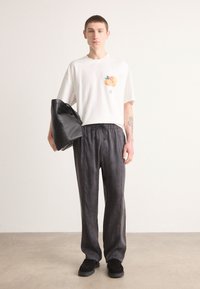 Hvit grafisk t-skjorte med et design av en fersken på brystet, parret med mørkegrå joggebukser med snøring og svarte slip-on sko. Svart totebag.