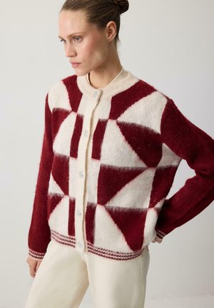 Cardigan à motifs rouges et crémeux en tissu doux, présentant des formes géométriques, un col rond et des fermetures à boutons avec des accents décoratifs.
