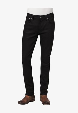 Schmal geschnittene schwarze Jeans mit Vordertaschen, getragen mit braunen Leder-Stiefeletten vor weißem Hintergrund.