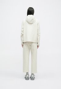 Haut à capuche beige clair, associé à un pantalon large assorti. Tissu doux et lisse avec une coupe décontractée, et chaussures de sport grises.