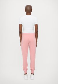 Roosad puuvillased joggersid soonikute külgedega, koos valge keha lähedal T-särgiga. Vaade on tagantpoolt, esitledes lihtsat disaini.