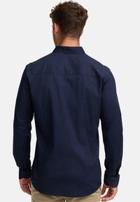 Camisa de manga larga azul marino con espalda recta, puños abotonados y una textura suave; presenta un cuello clásico y sin patrones visibles.