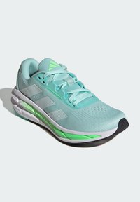 Zapato deportivo azul claro de material de malla con acentos verdes, superficie texturizada y suela de goma duradera que presenta una puntera negra.