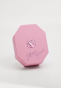 Boîte octogonale rose avec finition texturée, présentant un logo de cygne et "Ariana Grande" en lettres brillantes en relief.