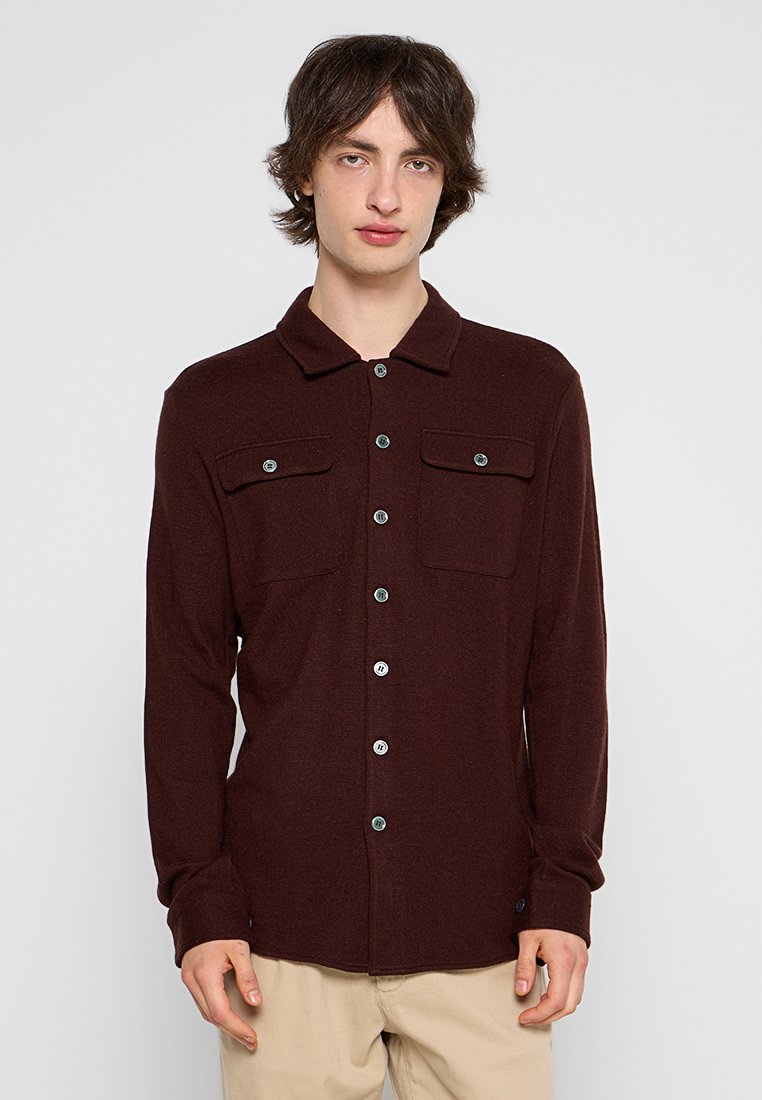 Bruine button-up shirt gemaakt van een zachte stof, met een kraag, twee borstzakken en contrasterende blauwe knopen. Lange mouwen.