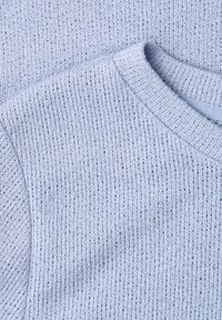 Tissu de pull tricoté bleu clair montrant l'encolure et le motif de points texturé en gros plan.