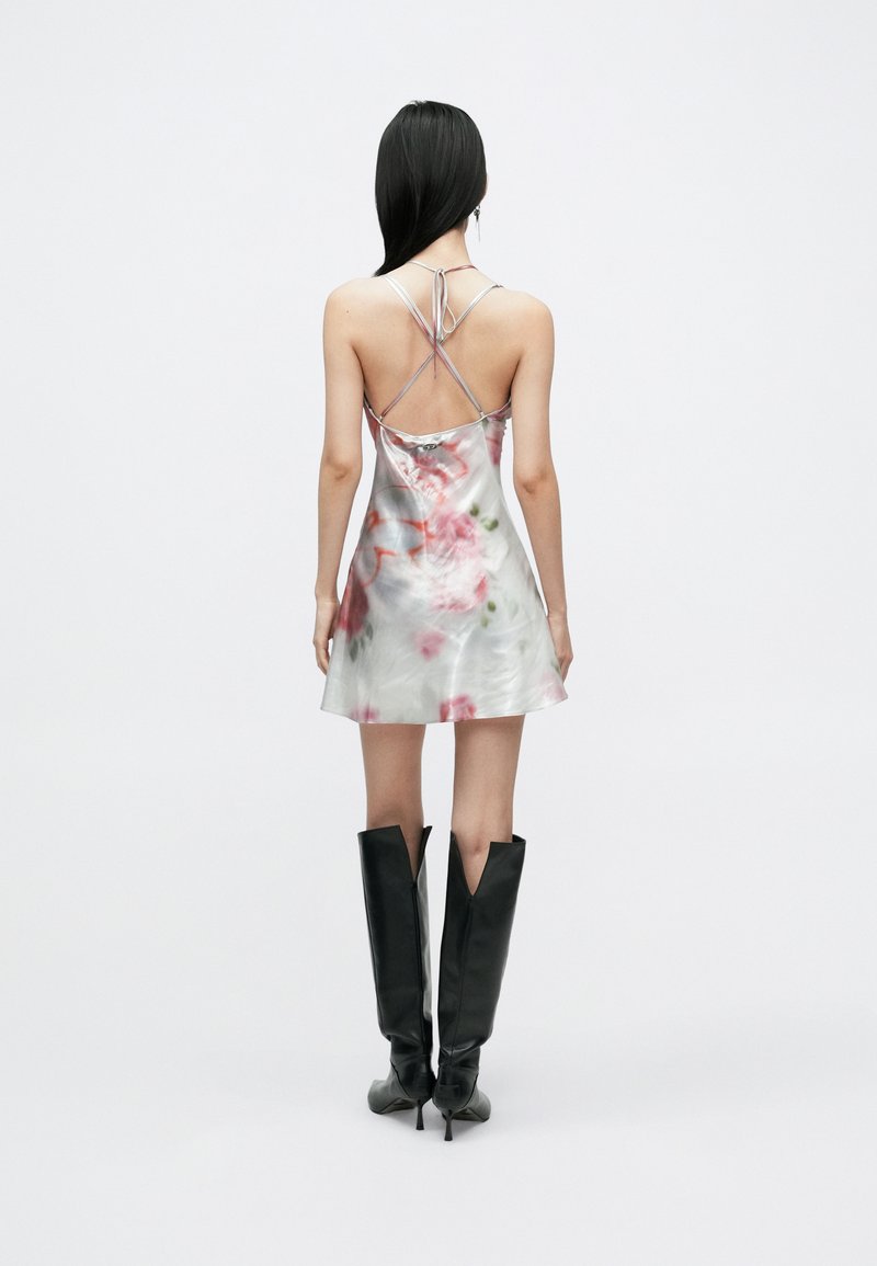 Satin slip dress with floral design in pink and green tones. Features crisscrossed straps and a flared hem. Paired with knee-high black boots.